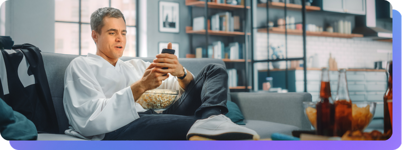 Man sitting on couch watching sports looking at sports app for stats and scores