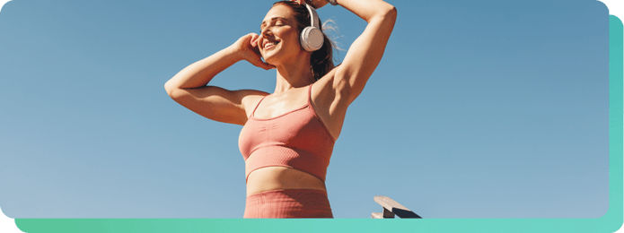 Woman in athletic wear smiling and listening to music through headphones after a workout, representing the emotional engagement music brings to fitness experiences.