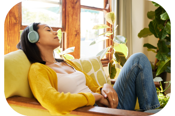 Woman laying in sun on couch listening to relaxing music on headphones