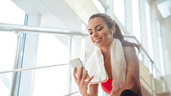woman getting ready to workout music listening on earbuds looking at phone fitness towel around neck